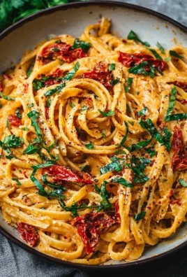 Creamy vegan pasta with sun-dried tomatoes garnished with leafy greens