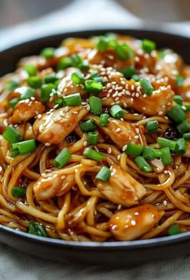 Plate of sticky garlic chicken noodles garnished with herbs.