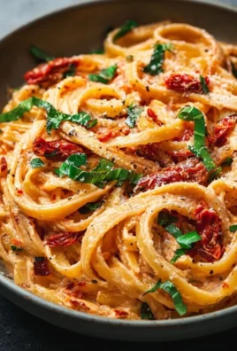 Bowl of vegan creamy sun dried tomato pasta garnished with fresh herbs
