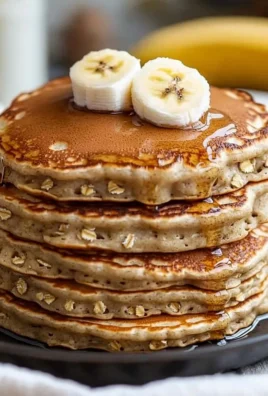 Delicious Banana Oats Pancakes stacked on a plate with syrup and bananas