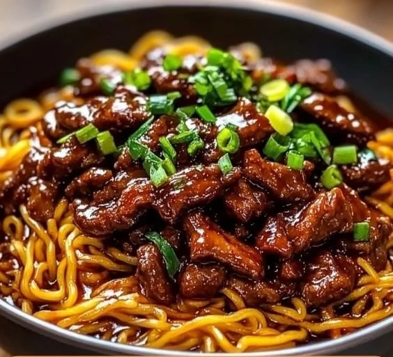 Plate of sticky beef noodles garnished with herbs and sauce.
